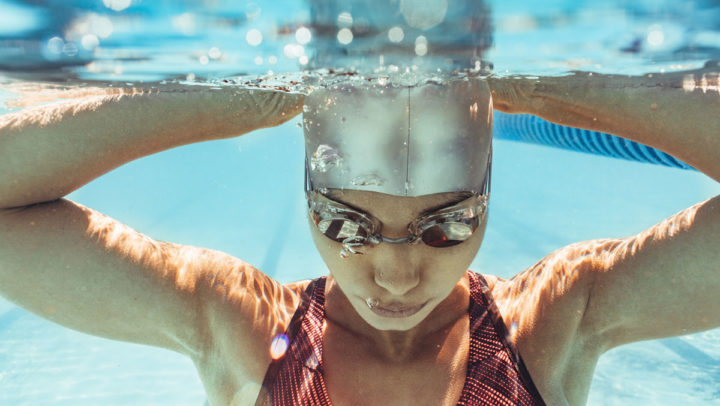 Kvinna med simglasögon och badmössa under vatten.